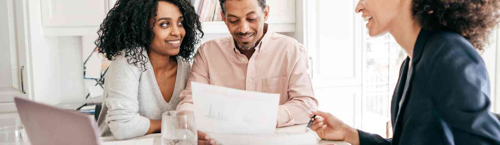 Two people sitting with a bank representative and reviewing paperwork.