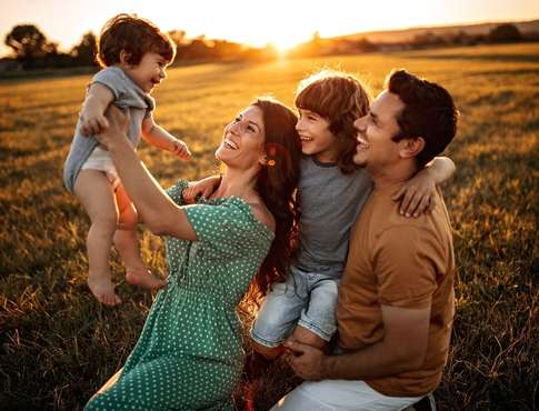 Happy family of four sitting in the field.